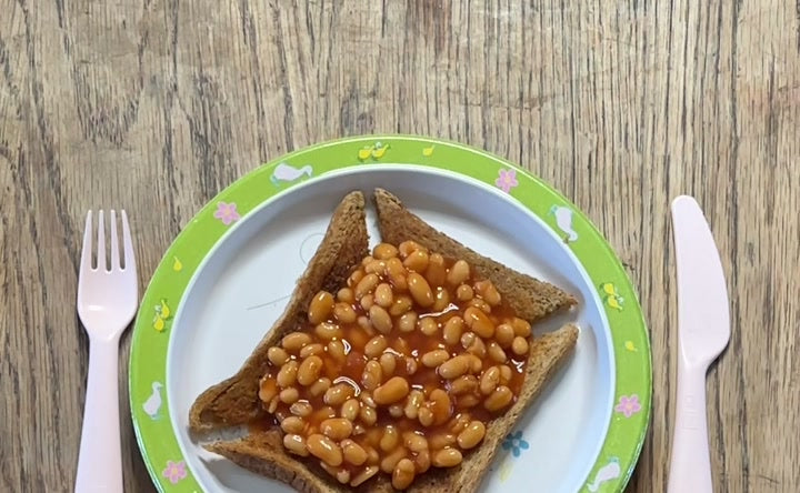 A child's plate of beans on toast on a wooden kitchen table